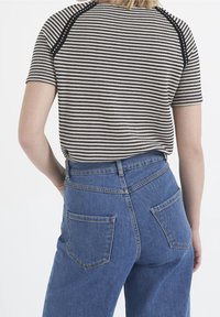 T-shirt en coton rayé noir et blanc à manches courtes, associé à un jean en denim bleu taille haute avec deux poches arrière.