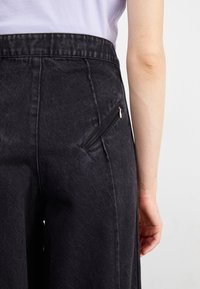 Črne denim hlače z visokim pasom, s stranskim žepom na zadrgo, gladko teksturo in ravnim krojem.