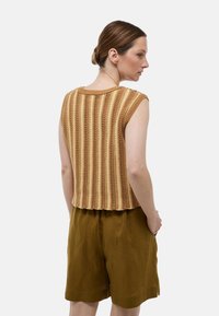 Un haut sans manches tricoté à rayures marron avec une texture côtelée, associé à un short en lin vert olive. Design simple et décontracté sans matériel visible.