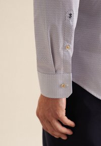 Himmelblaues gemustertes Hemd mit hexagonalem Design. Verfügt über Knopfmanschetten und einen einzelnen Knopfverschluss. Glattes Material, taillierte Passform.