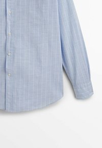 Chemise bleu clair à manches longues avec fines rayures verticales blanches et boutons blancs sur fond blanc uni.