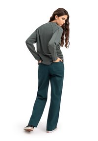 Camicetta a maniche lunghe verde scuro con scollatura rotonda e cuciture laterali, abbinata a pantaloni larghi color turchese e scarpe casual.