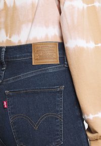 Jeans de mezclilla azul oscuro con un parche de cuero marrón que presenta "Levi Strauss & Co." Detalles de costura y diseño del bolsillo trasero visibles.