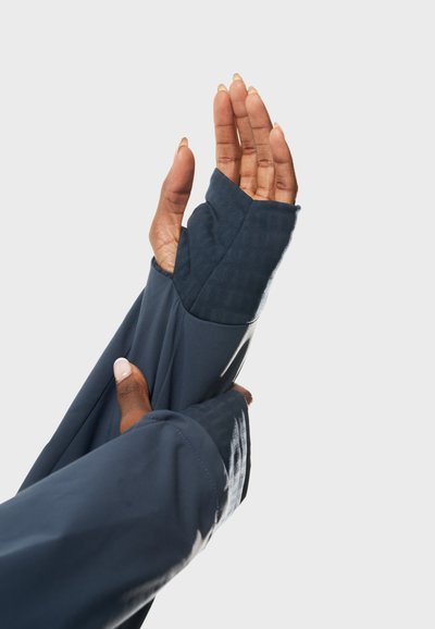 Långärmad, mörkblå plagg med fingerlösa manschetter och texturerade accenter. Slät tyg med en figurnära design som har ett hål för tummen.