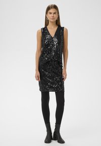 Fekete ujjatlan ruha, amelyet flitterek borítanak, V-nyakú, testhez simuló szabással, fekete harisnyával és bokacsizmával párosítva.