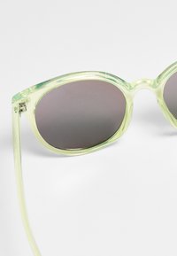 Occhiali da sole verde con montatura ovale oversized. Materiale plastico liscio e lenti scure. Presentano aste sottili e trasparenti.