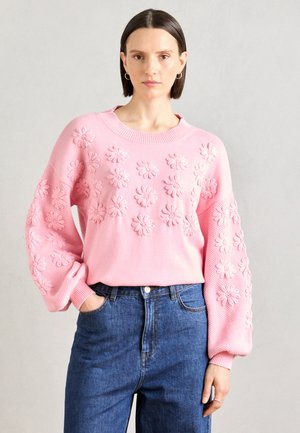 Pulover roz tricotat cu modele 3D de flori pe partea din față și mâneci texturate „balloon”, asortat cu blugi din denim cu talie înaltă.