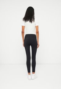 Svarta leggings med hög midja, som har en slät yta och åtsittande design. Bärs med en vit t-shirt med kort ärm och vita skor.