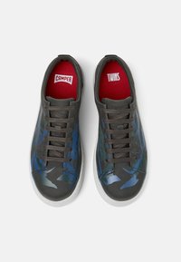 Graue Sneakers mit blauen Camouflage-Mustern, runder Zehenkappe, flacher Sohle, runden Schnürsenkeln und roten Innensohlen mit den Logos "CAMPER" und "TWINS".