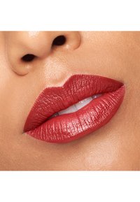 Une couleur de rouge à lèvres rouge profond avec une finition brillante, mettant en valeur la texture lisse et la forme définie des lèvres pulpeuses sur un fond de teint neutre.