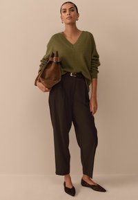 Olive green V-neck sweater, black wide-leg trousers, brown leather bag, and black flats with leopard print details. Smooth textures, relaxed fit.