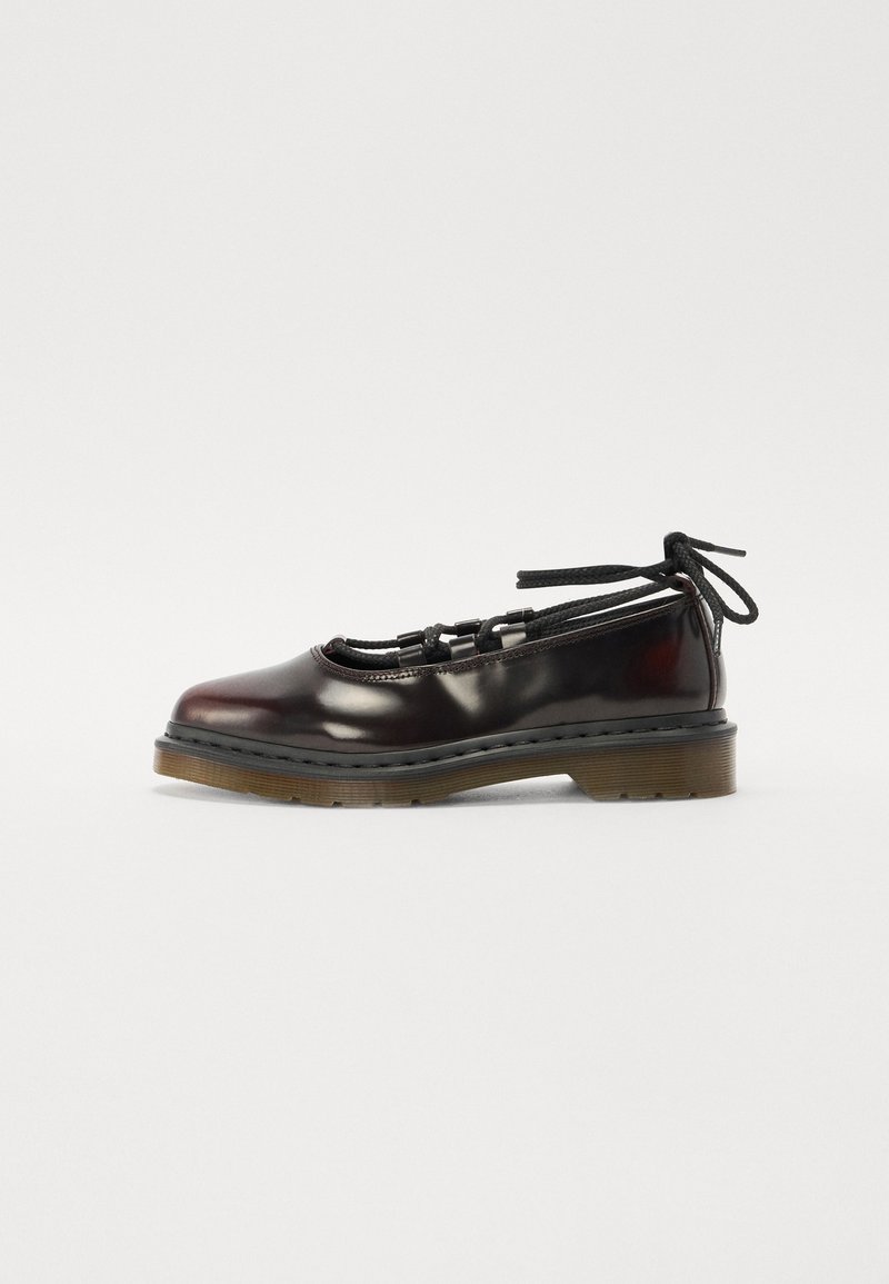 Chaussure plate en cuir noir à lacets, semelle épaisse marron et liens autour de la cheville, vue de côté sur fond blanc.