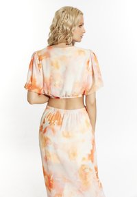 Completo a due pezzi con top corto e gonna lunga in tessuto leggero. Morbido motivo astratto ad acquerello in arancione e crema. Vita elastica.
