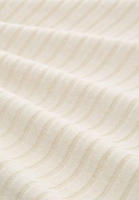 Cremefarbener Stoff mit einem gewellten Streifenmuster, das eine glatte Textur und einen dezenten Glanz aufweist. Die Nähte sind gleichmäßig entlang der Wellen verteilt.