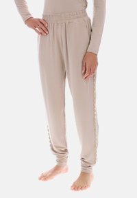 Lyse beigefarvede joggebukser med ribbet taljebånd, sidelommer og bølget kant langs benene, lavet af blødt, elastisk stof.