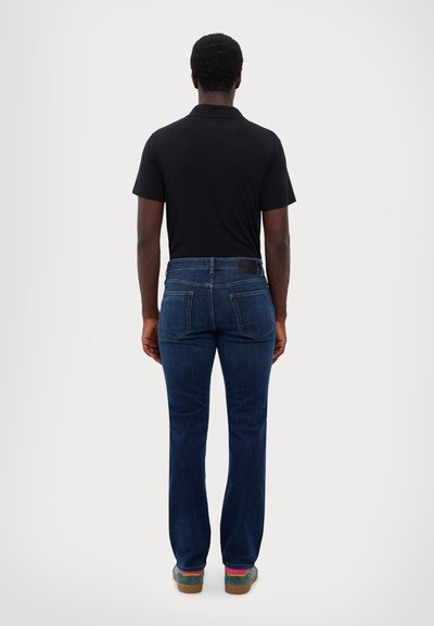 Dark blue denim jeans with a straight-leg cut, featuring two back pockets and a black leather waistband patch. Paired with a black polo shirt.