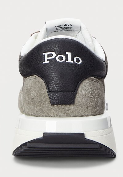Αθλητικό παπούτσι με μαύρη δερμάτινη φτέρνα, γκρίζο σουέτ σώμα και λευκές λεπτομέρειες. Φέρει το λογότυπο "Polo" στο πίσω μέρος και υφή στην επιφάνεια.