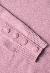 Manche de pull rose en tricot avec quatre boutons ronds assortis disposés en rangée près du poignet côtelé.