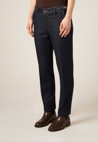 Pantalones vaqueros oscuros con pierna recta, dobladillo vuelto y costuras en contraste. Incluyen una cremallera lateral y un detalle de cadena metálica.