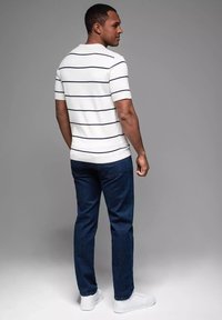 Kortärmad, vit polo med marinblå horisontella ränder, kombinerad med mörkblå jeans och vita sneakers. Vy från baksidan.