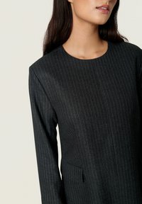 Fekete csíkos ruha kerek nyakkivágással, hosszú ujjakkal és oldalsó zsebbel. Simább textúra és szabott fazon. Nincsenek látható záródások.