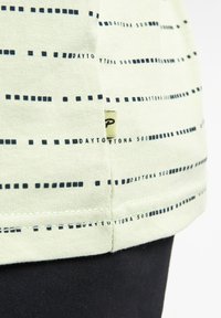 Camiseta verde claro con estampado geométrico en navy y texto "DAYTONA 500". Presenta una pequeña etiqueta de la marca cosida en el dobladillo. Tejido de algodón suave.