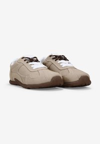 Zapatillas deportivas beige con textura de ante, cordones blancos y suela marrón. Presenta puntera redondeada y detalles en el panel lateral.