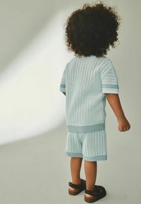Ensemble tricoté bleu clair en deux pièces comprenant des manches courtes et un short, tous deux avec un motif texturé. Porté avec des sandales noires.