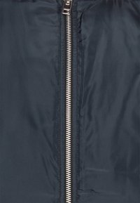 Gros plan d'une veste en tissu noir avec une fermeture éclair métallique argentée au centre, partiellement ouverte.