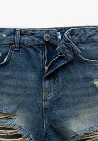 Shorts de mezclilla en azul claro con desgastes y roturas, cierre de botón metálico, cremallera y detalles en costura naranja. Incluye múltiples bolsillos.