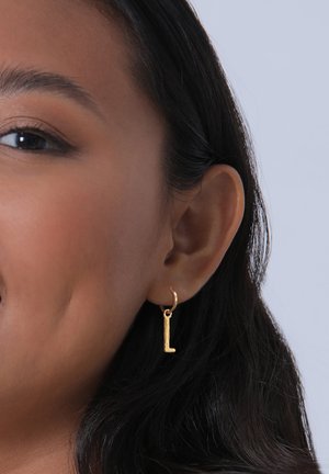 Guld hoopørering med en tekstureret charms i form af bogstavet "L", ophængt for øget visuel detaljer. Sat mod en neutral baggrund.