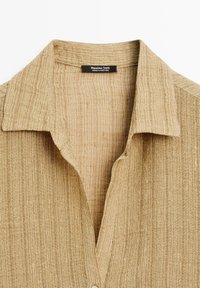 Camicia beige con bottoni, realizzata in un tessuto a costine testurizzato e colletto classico. L'etichetta riporta "Massimo Dutti, Made in Portugal."