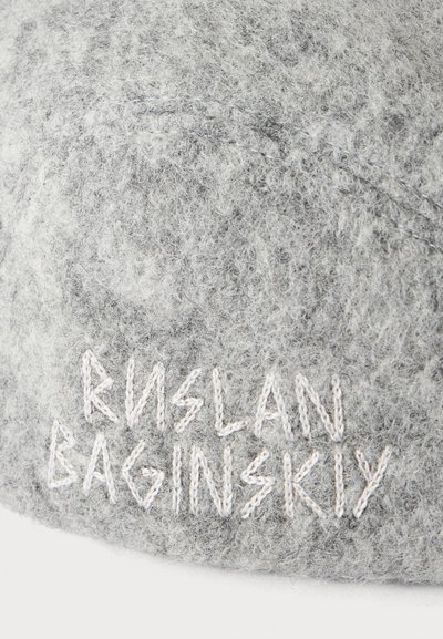 Γκρίζο μαλακό ύφασμα με λευκό κεντητό κείμενο που γράφει "KISLAN BAGINSKIY" και μια αχνή καμπυλωτή γραμμή πάνω από το κείμενο.