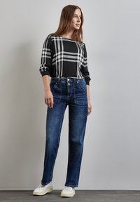 Sort og gråternet langærmet top parret med højtaljede blå jeans med forlommer, afsluttet med hvide sneakers.