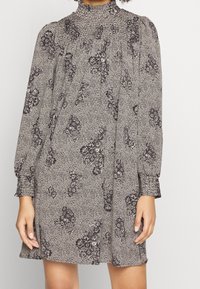Blumenmusterkleid in Schwarz und Weiß, mit hohem Kragen, langen Ärmeln und lockerer Silhouette. Es hat zarte Punktmuster und geraffte Details.