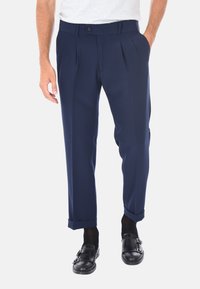 Pantaloni a pieghe blu realizzati in un tessuto liscio, dotati di vita aderente e orli a risvolto, abbinati a scarpe nere slip-on.