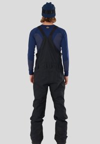 Czarne izolowane spodnie ogrodnicze z regulowanymi szelkami, noszone na granatowej bluzie z długim rękawem z paskami, odpowiednie do aktywności w zimnej pogodzie.