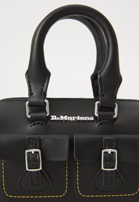Zwarte leren handtas met twee gespzakken, gerolde handvatten, gele stiksels en zilveren Dr. Martens-logo aan de voorkant.