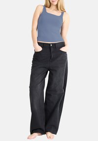 Ljusblå ärmlös topp med breda axelband, kombinerad med högmidjade svarta vida jeans med framknäppning och sidfickor.