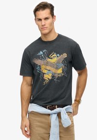 T-shirt en coton noir avec un graphique coloré représentant un oiseau et des éclairs, doté d'un col rond et de manches courtes.