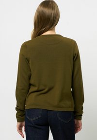 Olivgrön långärmad tröja med rund halsringning och ribbade manschetter och avslut. Slät textur och avslappnad passform, kombinerad med mörka jeans.