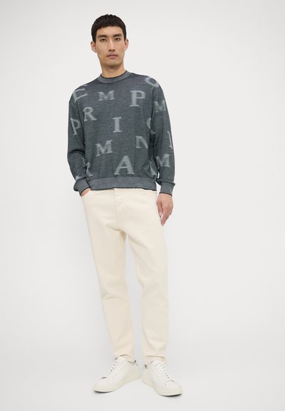 Maglione grigio con un motivo a logo ripetuto, scollatura rotonda e polsini a coste. Abbinato a pantaloni color crema e sneakers bianche.