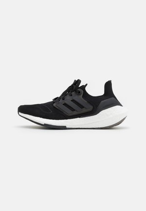 Chaussure de course Adidas Ultraboost noire avec tige en maille, lacets noirs, trois bandes sur le côté et semelle épaisse en mousse blanche.