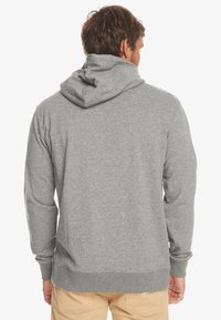 Grijze hoodie van zachte katoenmix, met een buidelzak, rib gebreide manchetten en een capuchon met drawstring. Achteraanzicht toont de gladde textuur.