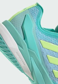 Jasnoniebieski but sportowy z teksturowanej tkaniny, z syntetycznymi dodatkami i jaskrawozielonymi detalami. Posiada sztywną podeszwę i wielokierunkowy bieżnik.