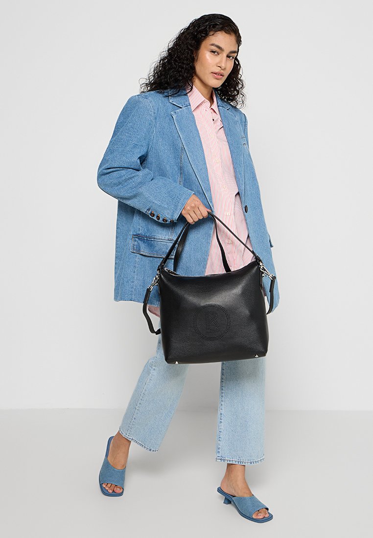Schwarze Lederhandtasche mit einem runden geprägten Logo, silbernem Beschlag und zwei Griffen, kombiniert mit einem Jeansblazer und hellblauen Jeans.