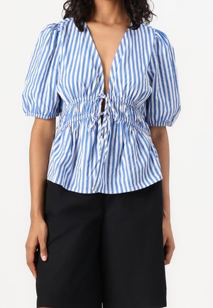 Blau-weiß gestreifte Bluse mit tiefem V-Ausschnitt, Puffärmeln und geraffter Taille mit Kordelzugdetail. Kombiniert mit schwarzen Shorts.