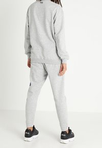 Gray sweatshirt and matching joggers made of soft material, featuring ribbed cuffs, logo detail, and black sneakers.