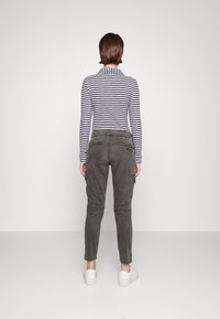 Gestreiftes Langarmshirt in Marineblau und Weiß, kombiniert mit olivgrünen Cargo-Hosen mit Seitentaschen und umgeschlagenen Saum, getragen mit weißen Sneakers.