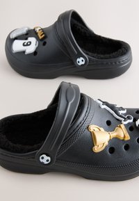 Saboturi negre cu interior pufos, decorate cu tematică de fotbal, inclusiv un trofeu, un tricou și accente în formă de jucător.